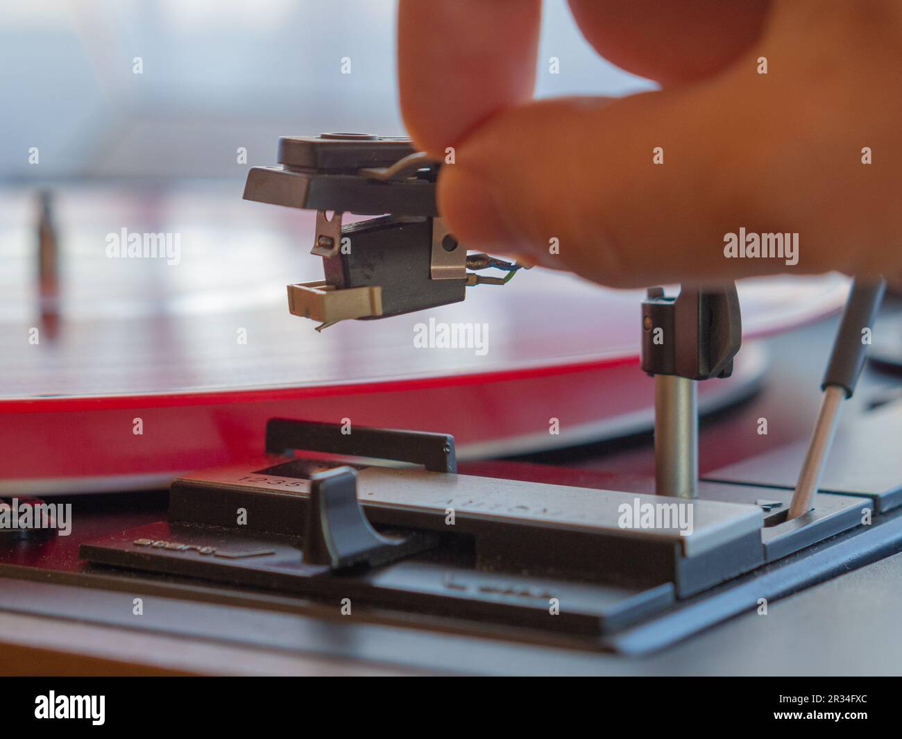 Détail d'une main masculine plaçant l'aiguille sur la piste d'un disque en vinyle rouge. Plateau tournant vintage Banque D'Images