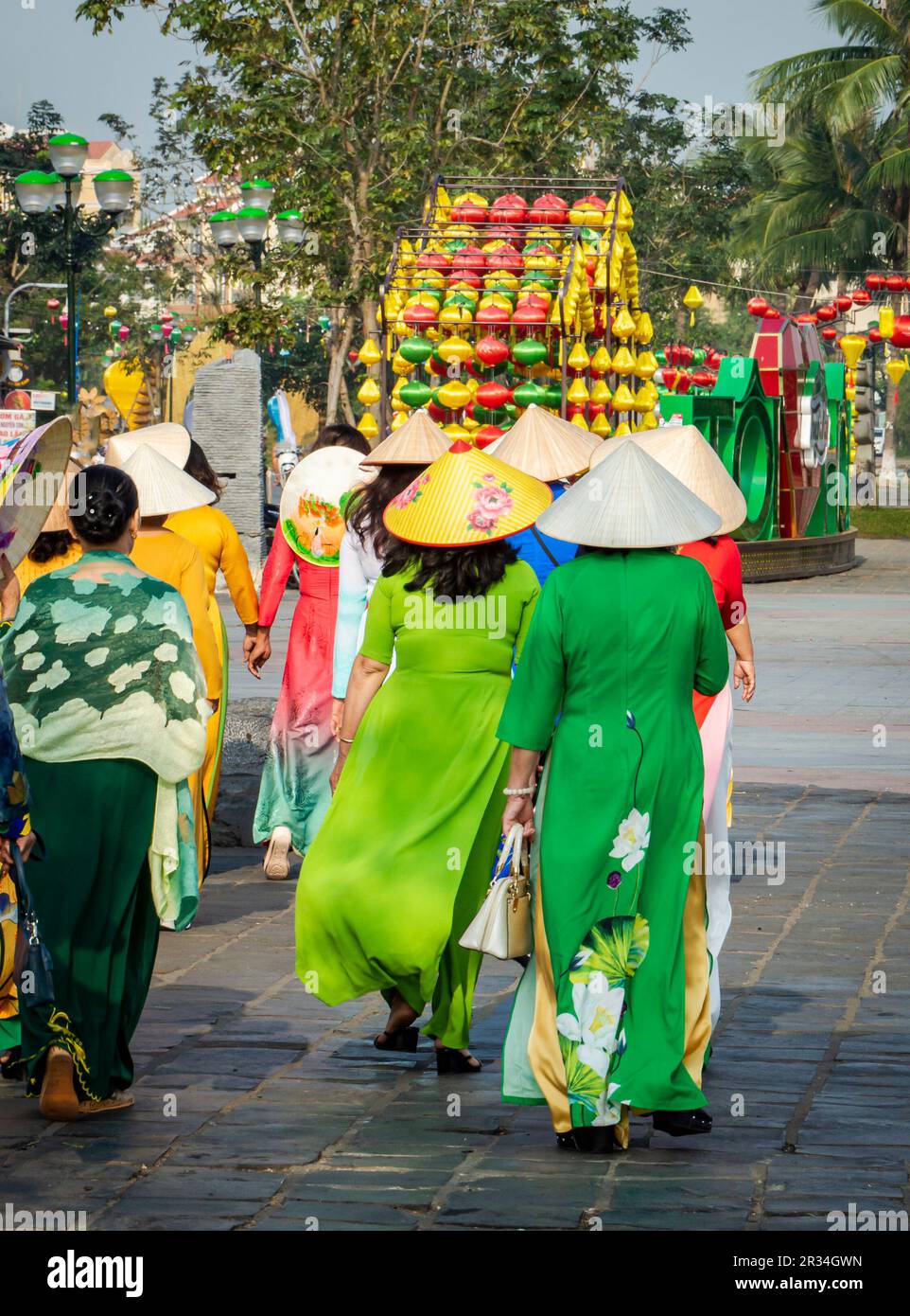 Vue arrière d'un groupe de femmes portant des robes traditionnelles vietnamiennes marchant dans la vieille ville de Hoi an par une journée ensoleillée. Banque D'Images