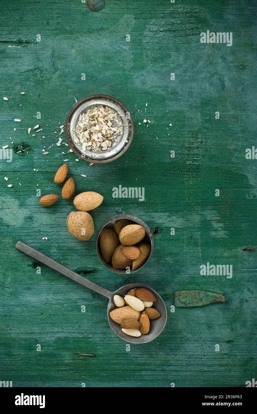 Amandes, décortiquées et non décortiquées, sur une cuillère et dans un bol, surface en bois rustique avec amandes effilées Banque D'Images