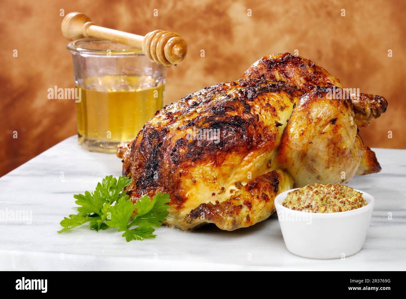 Un poulet rôti entier cuit avec un glaçage au miel et à la moutarde, avec un plat de moutarde, un pot de miel et un sèche-miel Banque D'Images