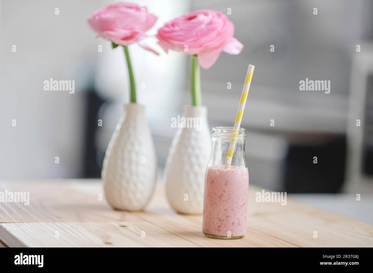 Lait de framboise avec une paille en bouteille et fleurs de ranunculus roses en deux vases Banque D'Images