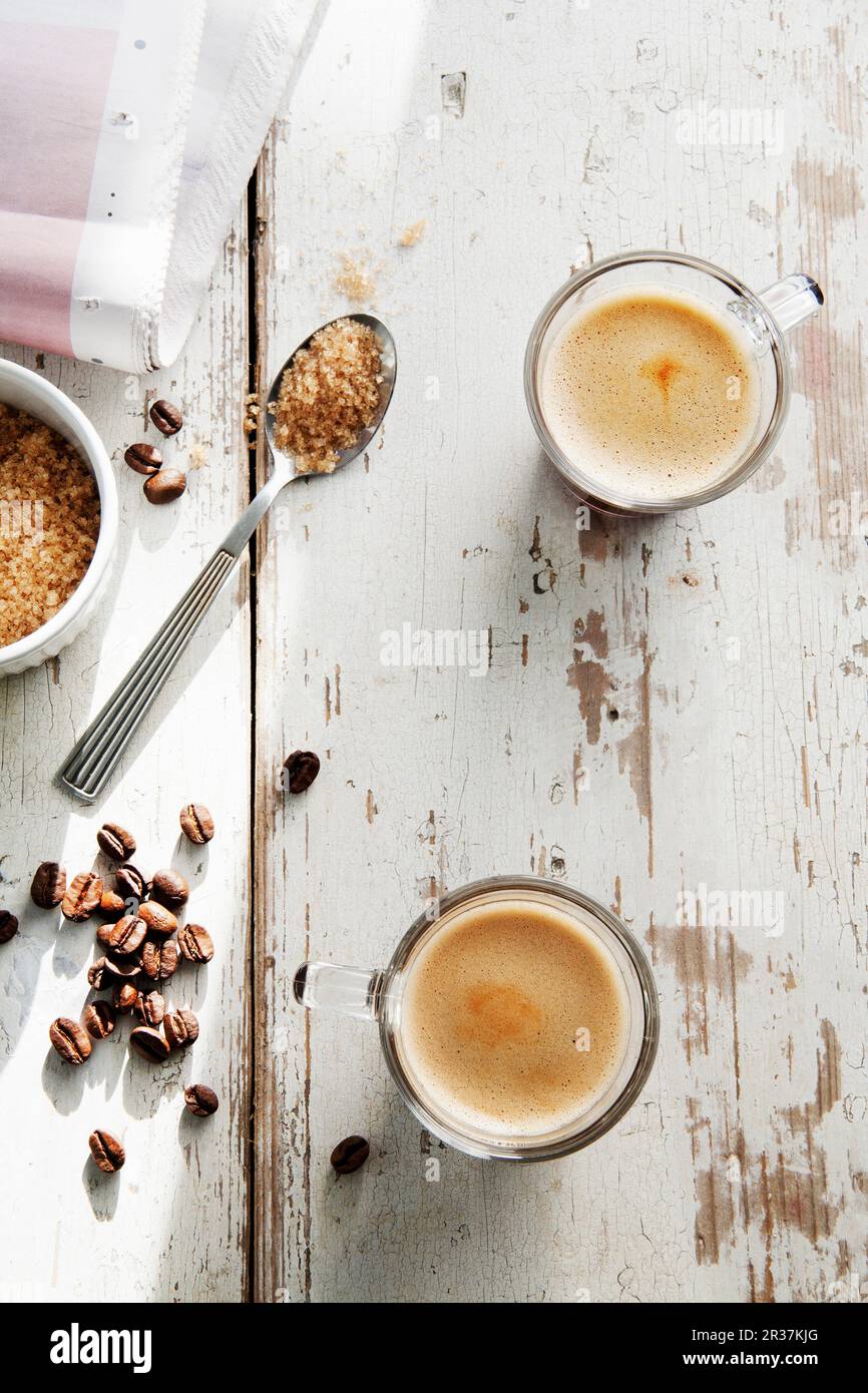 Les grains de café, une cuillère à café de sucre brun et deux tasses d'expresso sur une table blanchis Banque D'Images