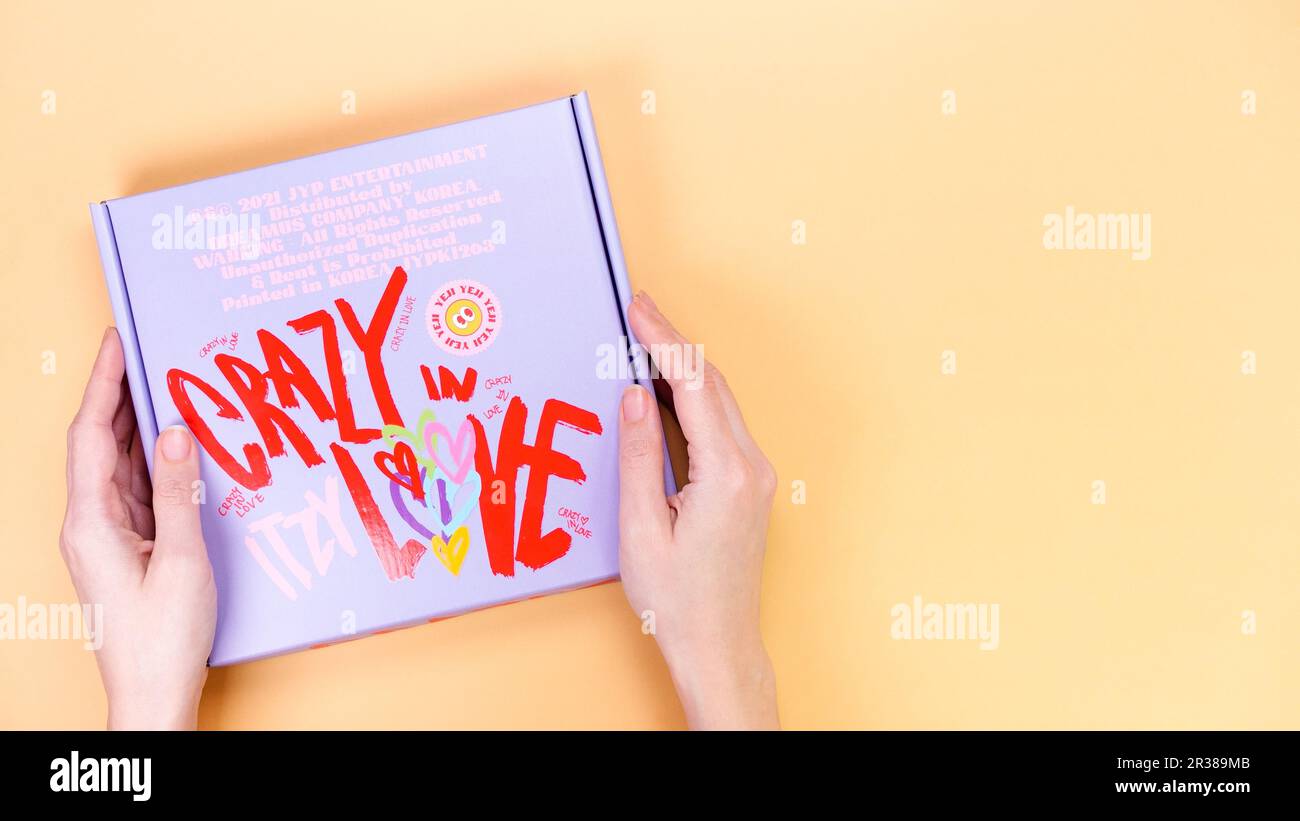 Mains tient K-pop groupe Itzy FOU DANS L'AMOUR album 1st sur fond jaune. CD de musique en édition spéciale. Groupe de filles sud-coréennes Itzy. Espace pour le texte. GAT Banque D'Images