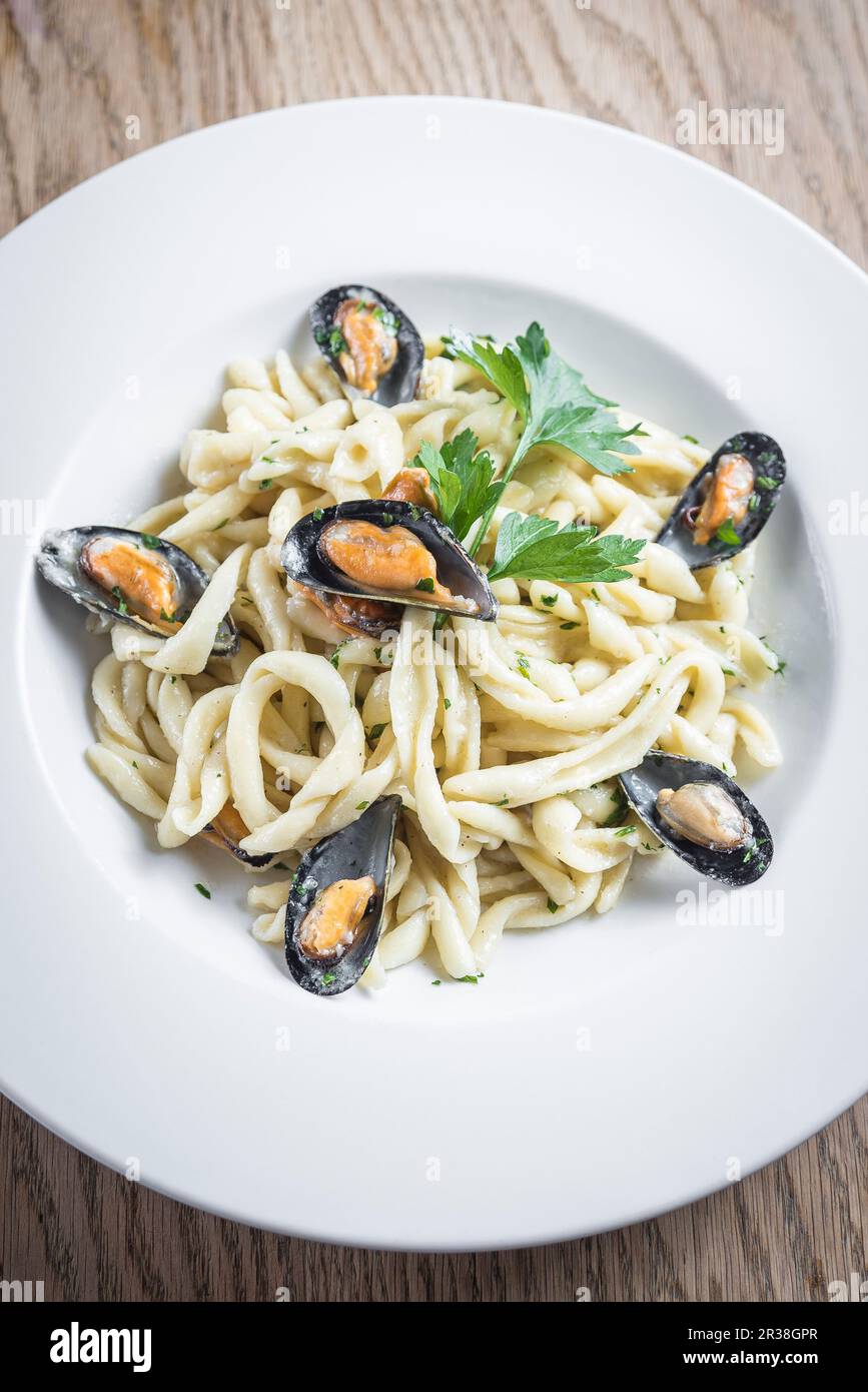 Pâtes fraîches artisanales traditionnelles avec moules et sauce crémeuse au fromage pecorino, garnies de persil dans une assiette blanche Banque D'Images