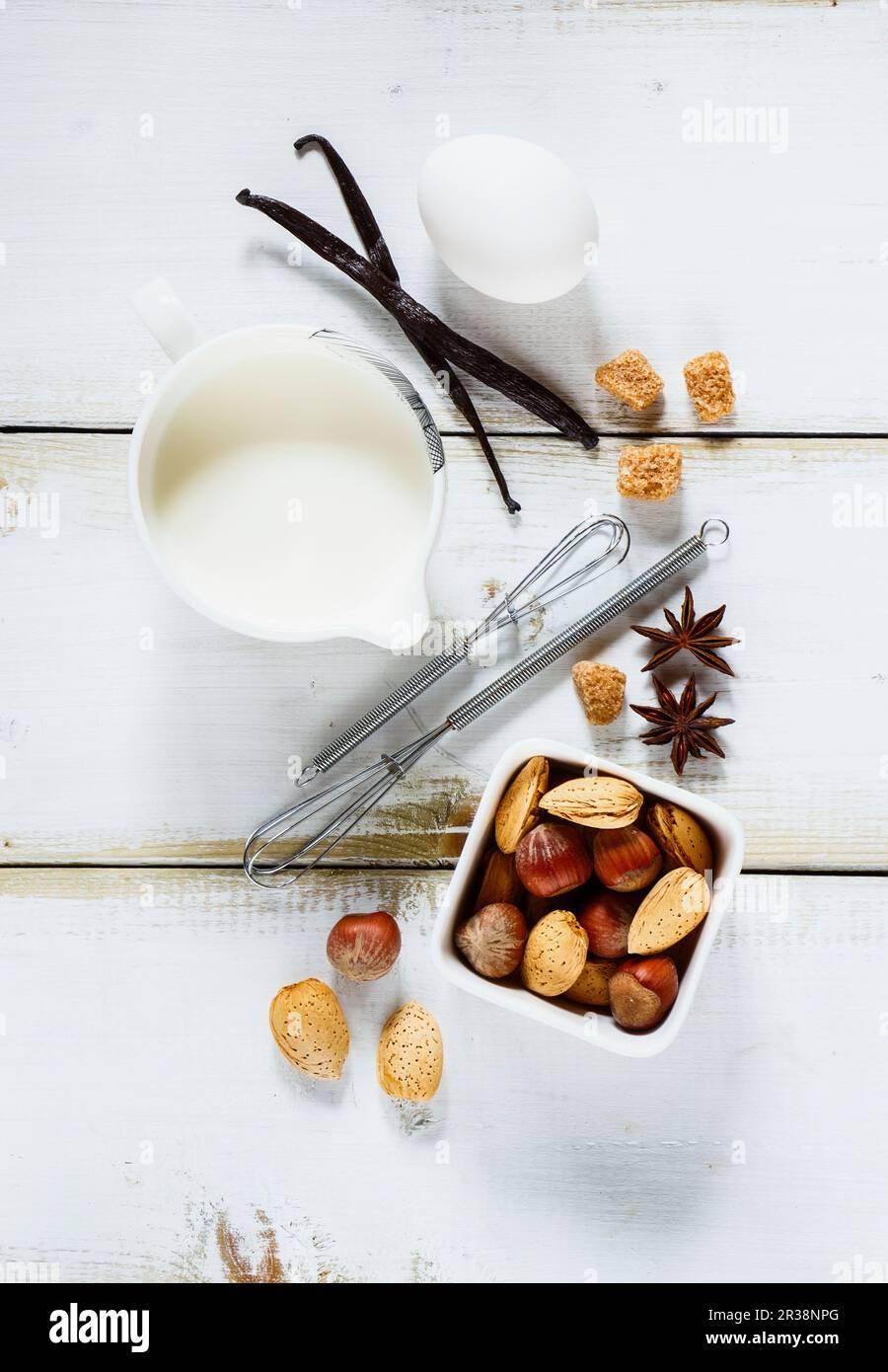 Pétrissez les ingrédients de la recette (œuf, lait, sucre, noix, bâtonnets de vanille et de cannelle) sur fond de bois blanc Banque D'Images