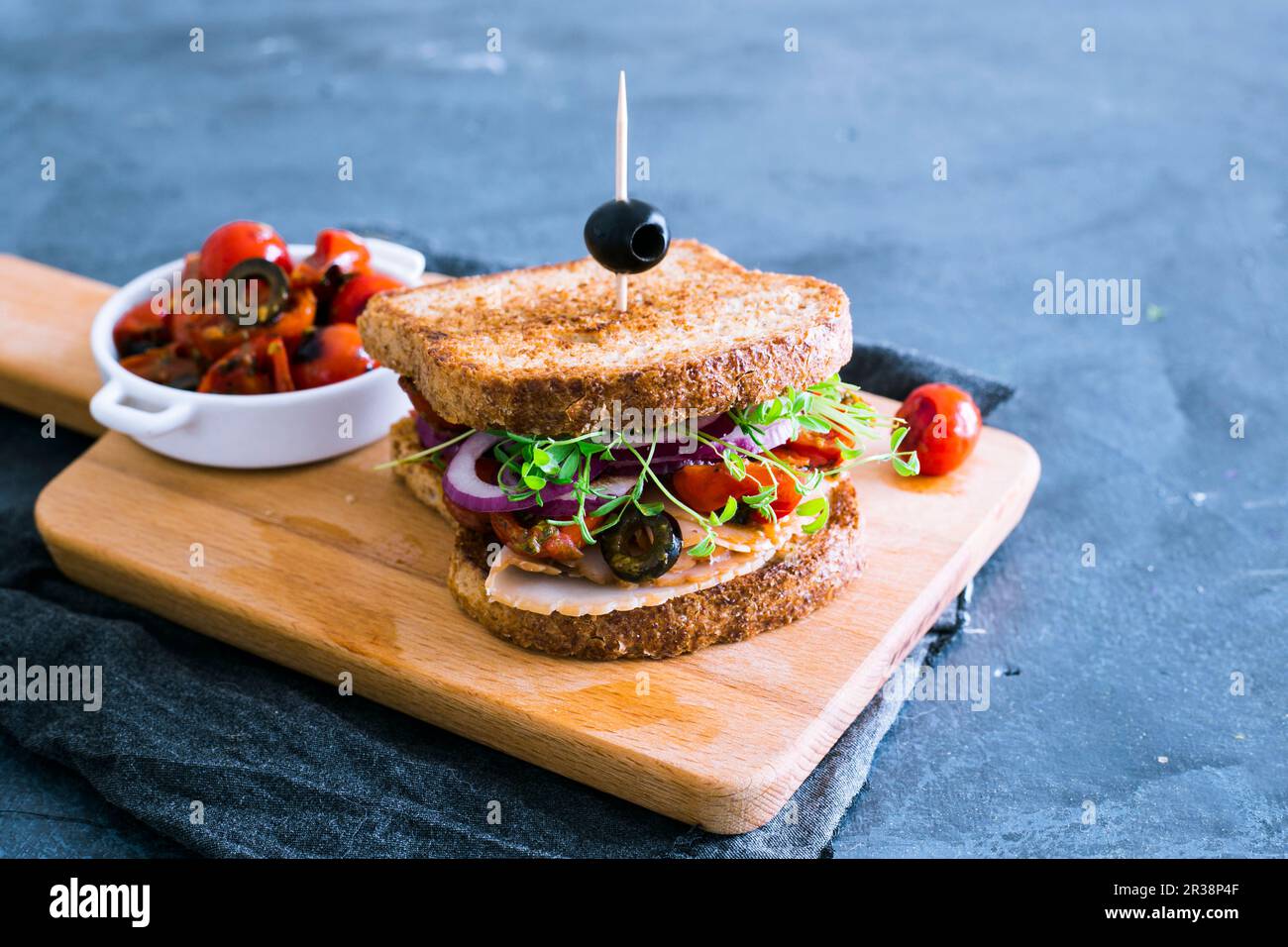 Un sandwich à la dinde avec du pesto, des pousses, des olives, des tomates cerises et des oignons Banque D'Images