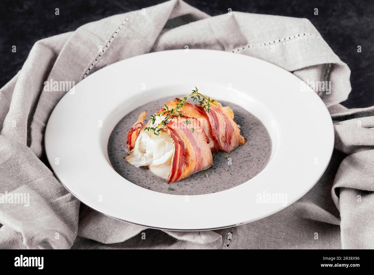 Assiette avec filet de poisson à la ligne cuit, enveloppé dans du bacon, sur des haricots noirs et de la crème de pomme de terre Banque D'Images