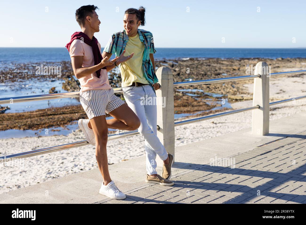 Heureux biracial gay couple masculin parlant sur la promenade au bord de la mer Banque D'Images