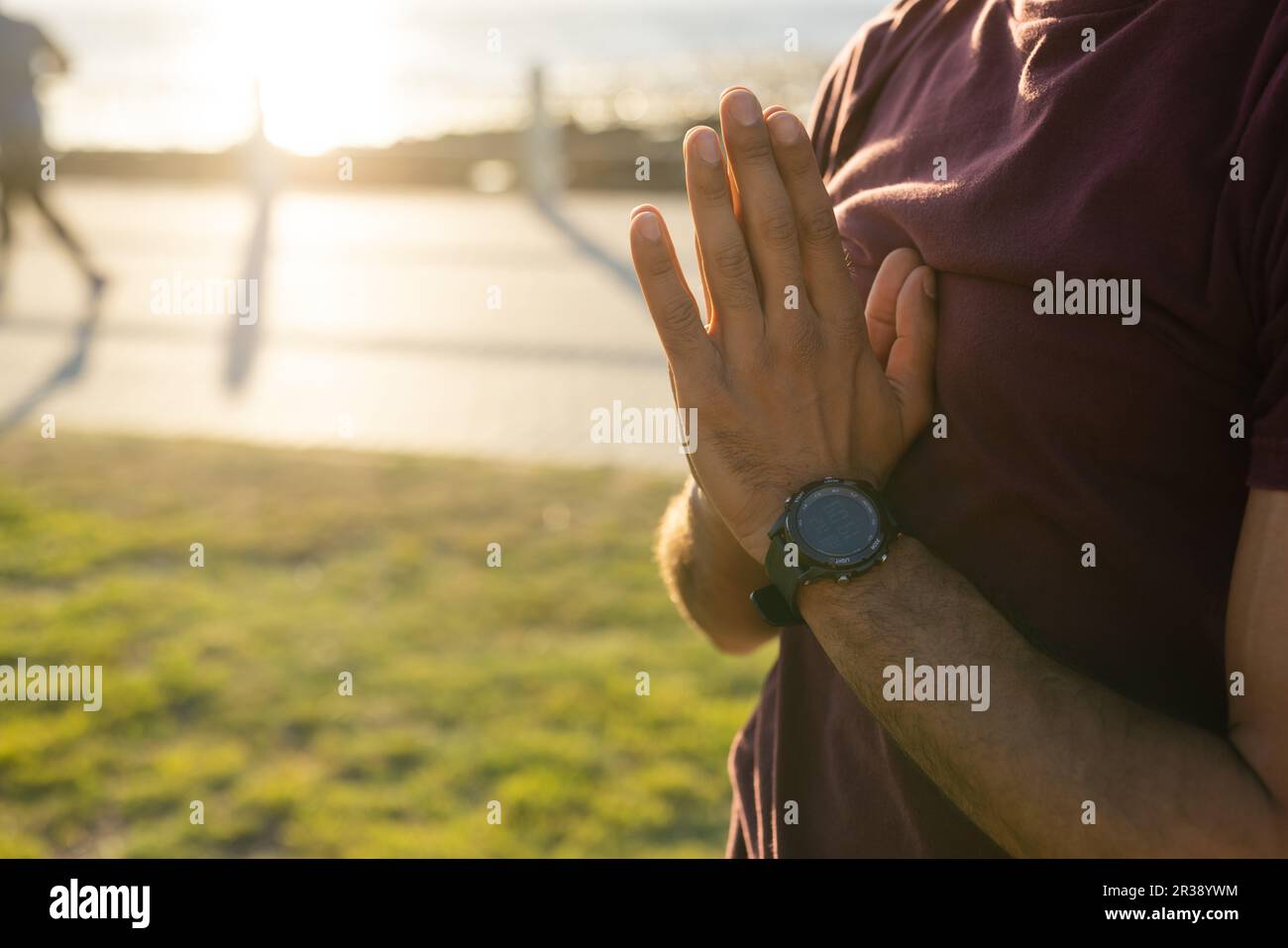 Section médiane de l'homme biracial faisant du yoga avec les mains dans la pose de prière, sur la promenade au coucher du soleil, espace de copie Banque D'Images