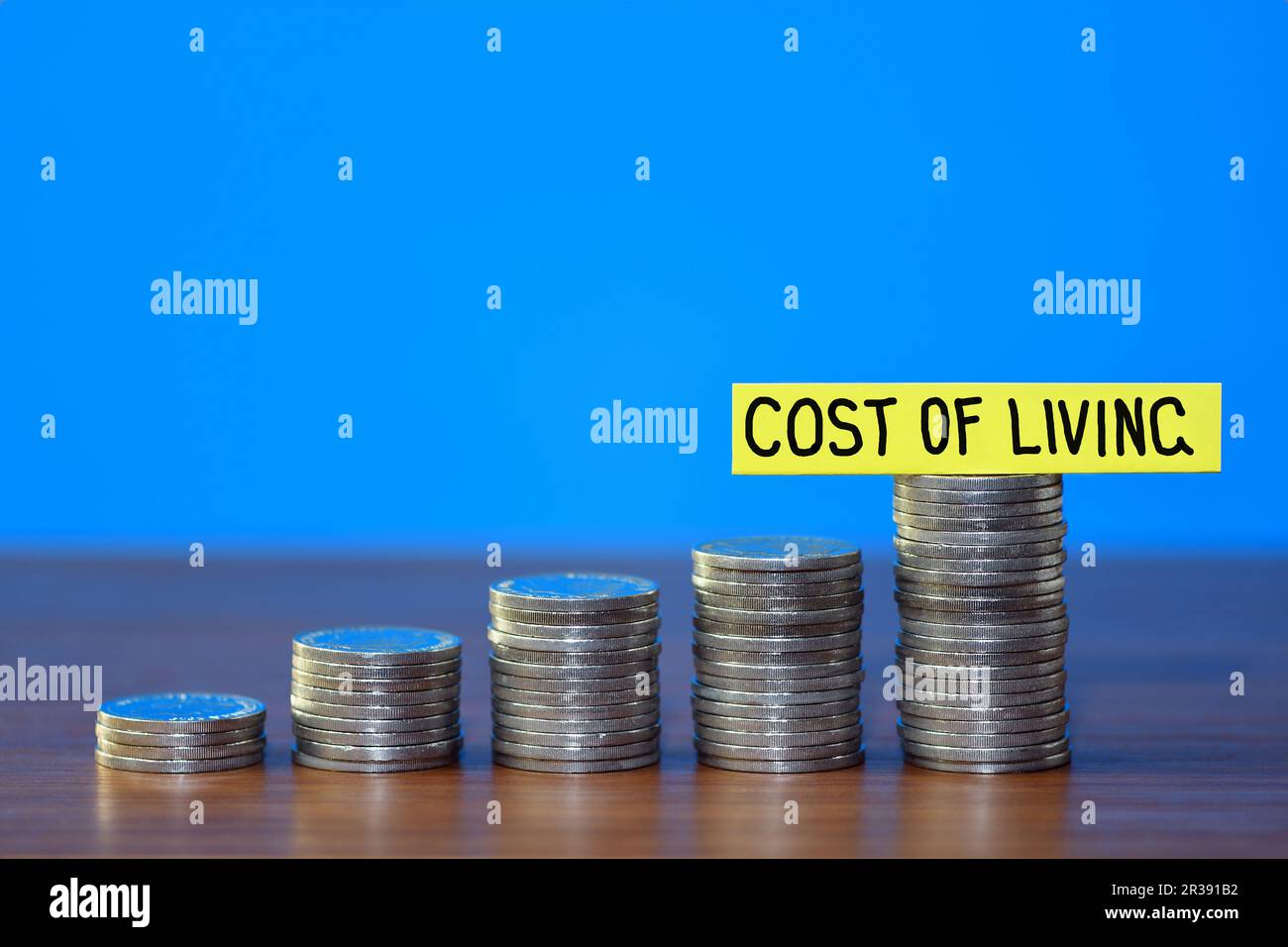 Une rangée d'une pile croissante de pièces illustrant la hausse du coût de la vie, sur un fond bleu avec l'espace de copie au sommet, concept Banque D'Images