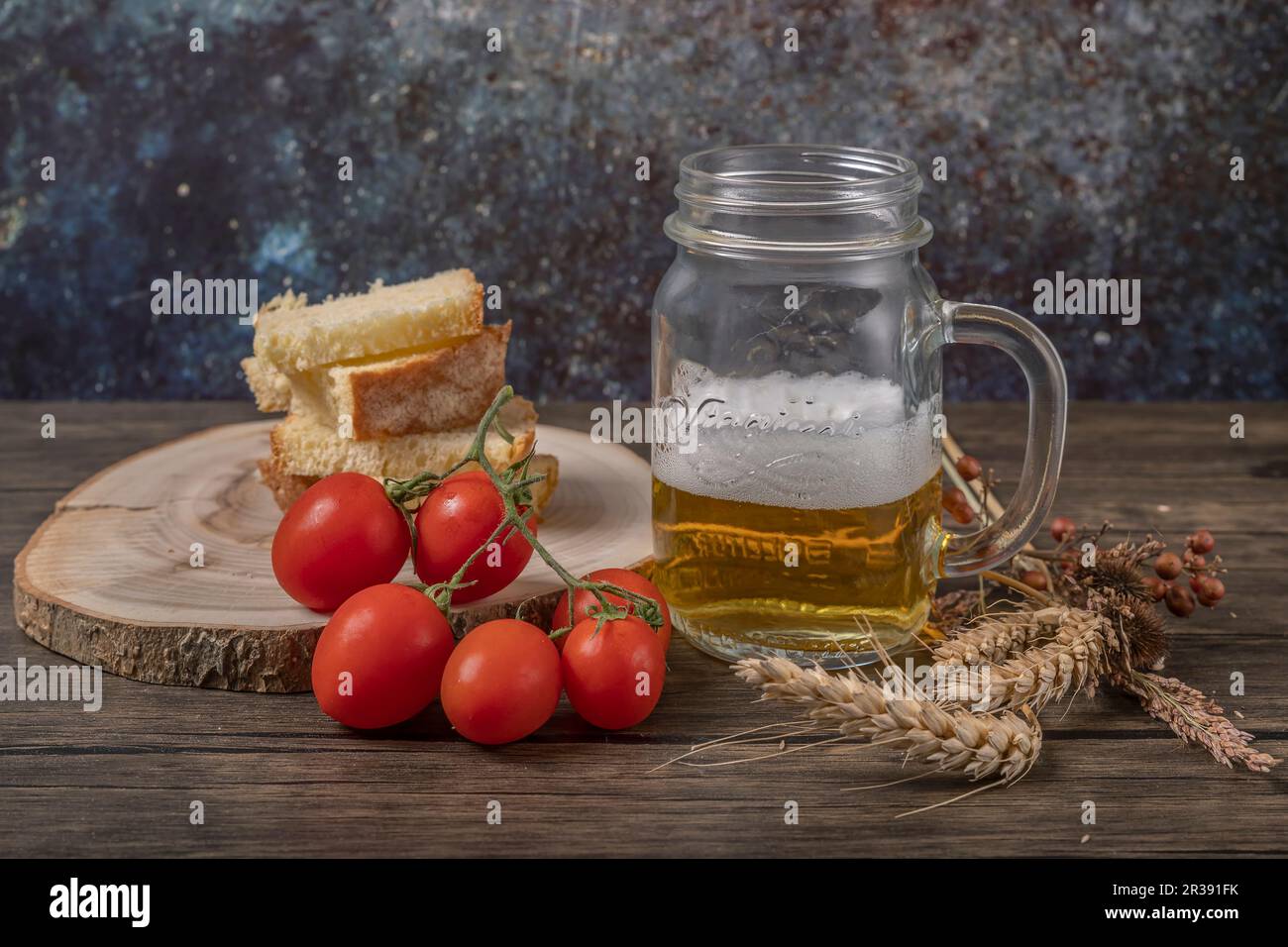 Une tasse de bière avec du pain grillé et des tomates cerises rouges à côté, avec des épis de maïs séchés Banque D'Images
