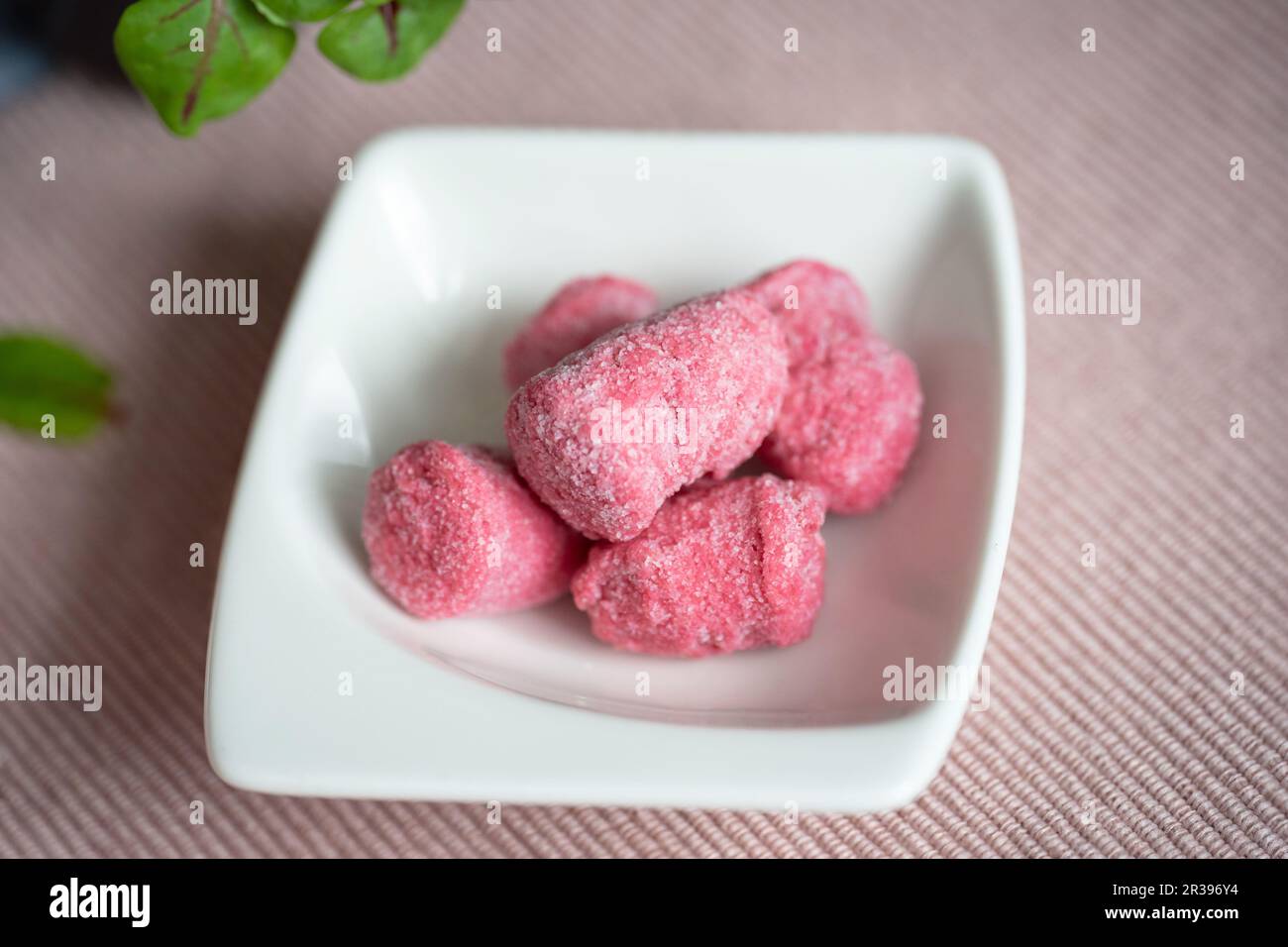 Gnocchi rose encore congelé (betterave) dans un petit bol blanc sur le tissu rose de la table. Banque D'Images