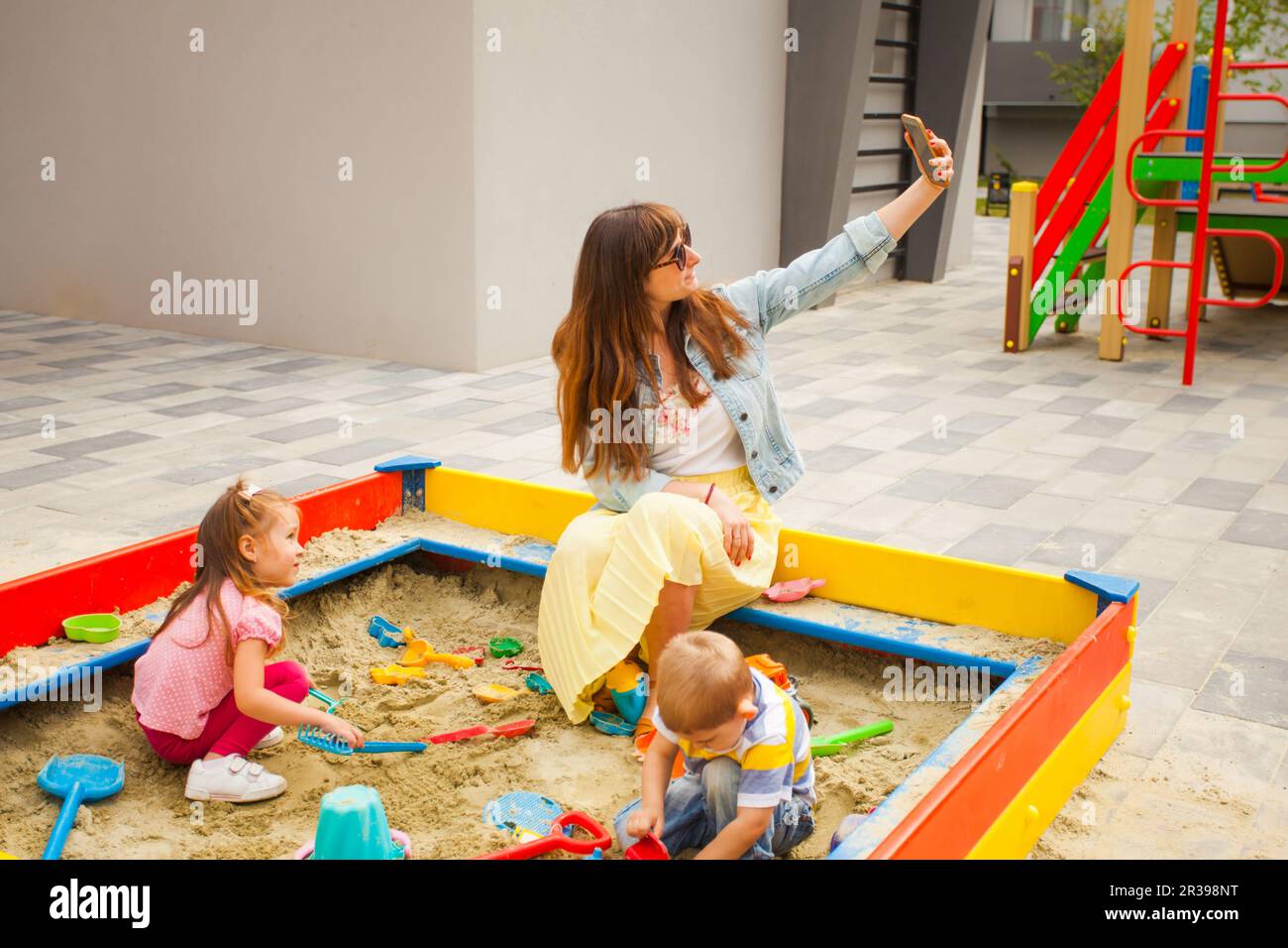 Mother sitting avec enfants en sandbox et utilisation du téléphone Banque D'Images