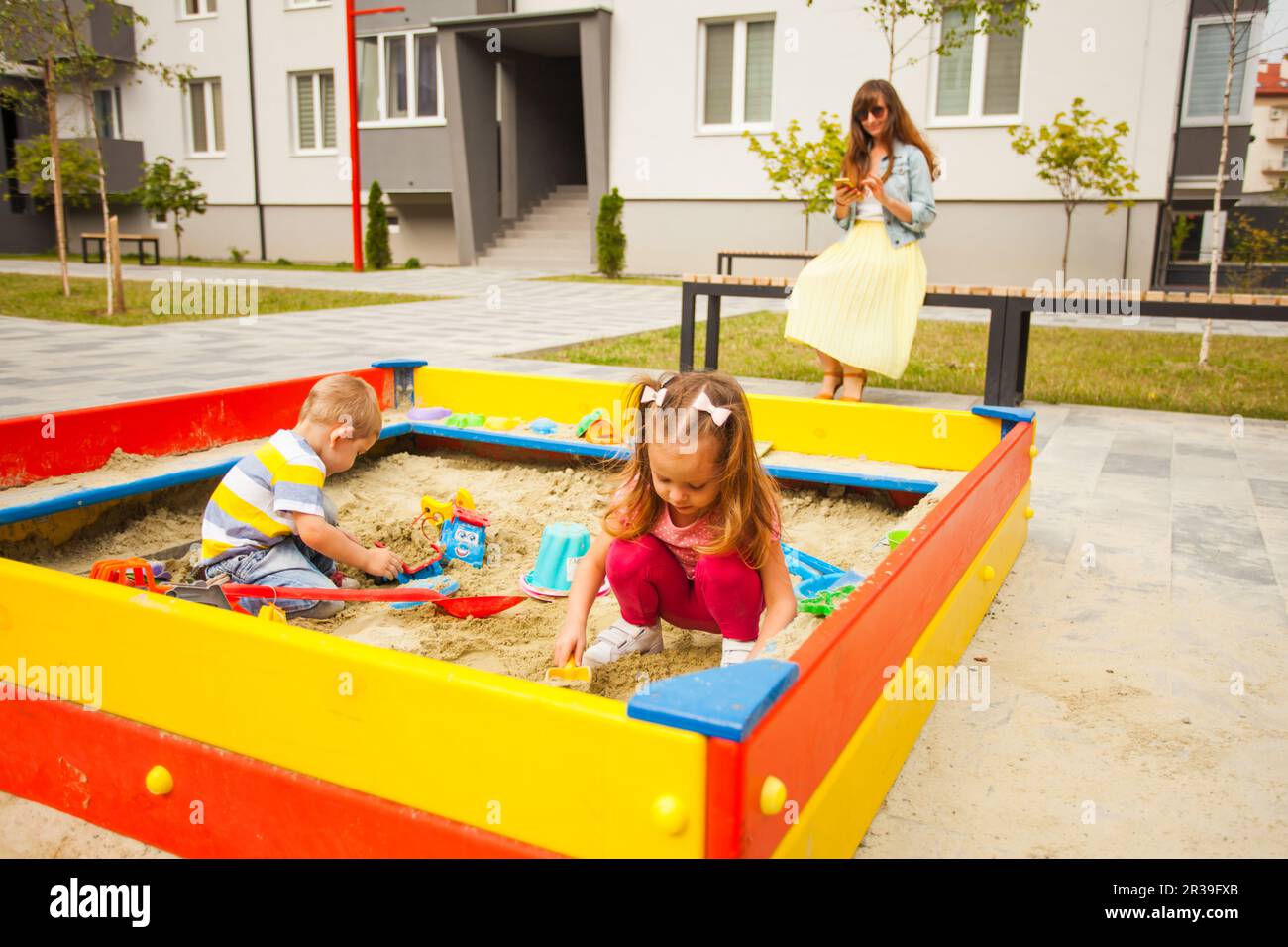 Petits enfants jouant dans un sandbox moderne avec des jouets. Jeune famille heureuse à pied. Banque D'Images
