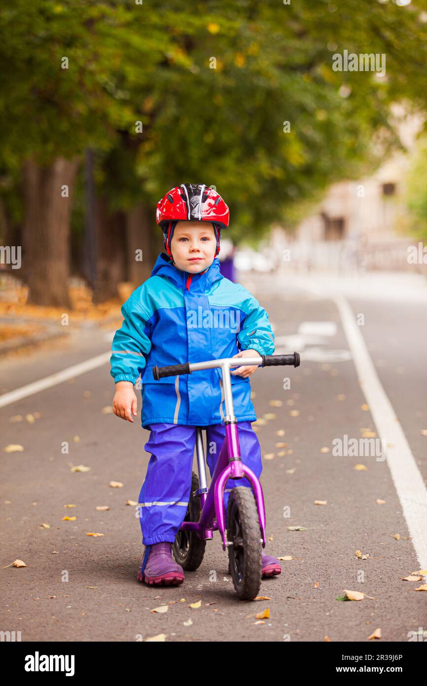 Garçon dans une veste chaude qui s'est assis sur son vélo d'équilibre Banque D'Images