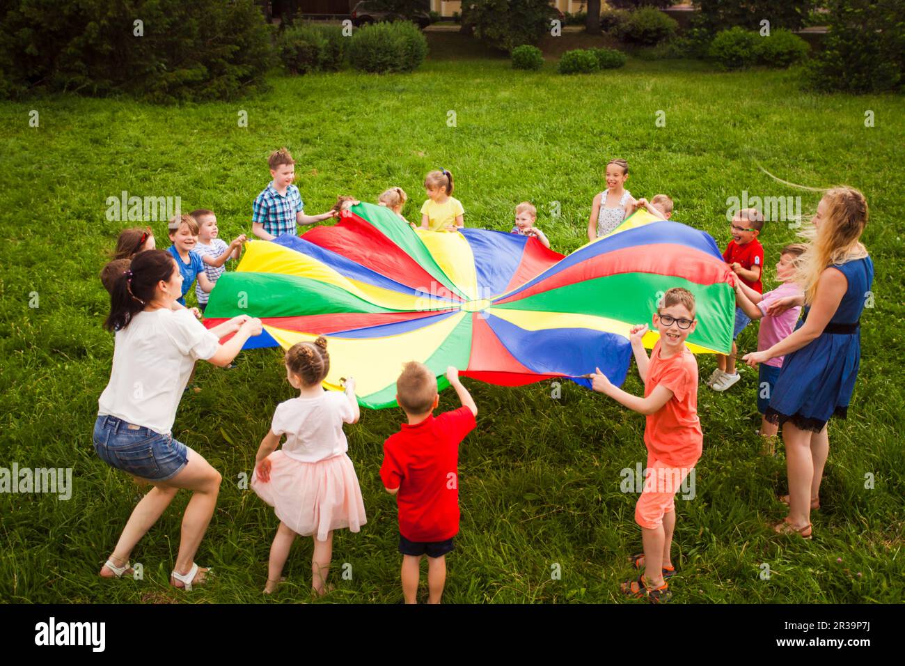 Enfants jouant avec le parachute arc-en-ciel dans le parc Banque D'Images