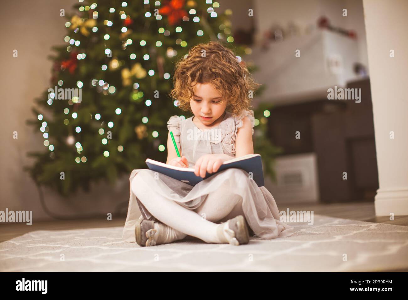 Petite fille assise à côté de l'arbre festif et dessin Banque D'Images