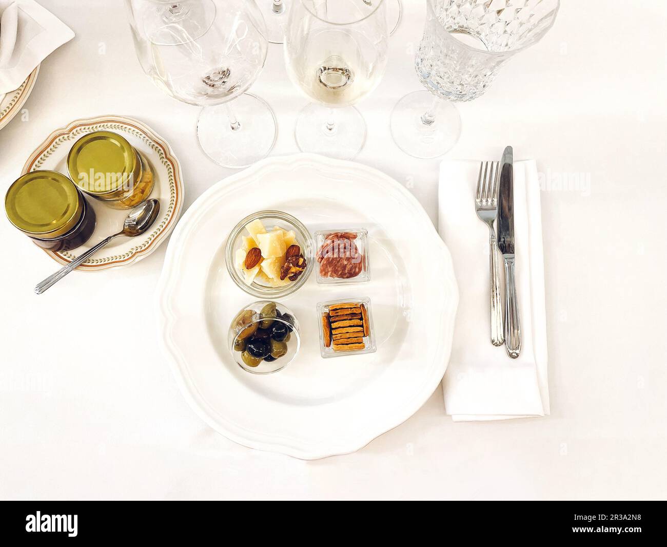 Assiette en porcelaine blanche avec délicieux en-cas. Olives, fromage, amandes, jambon en verre séparé bowles. Verres de champagne vides. Pots de conservation sur p Banque D'Images