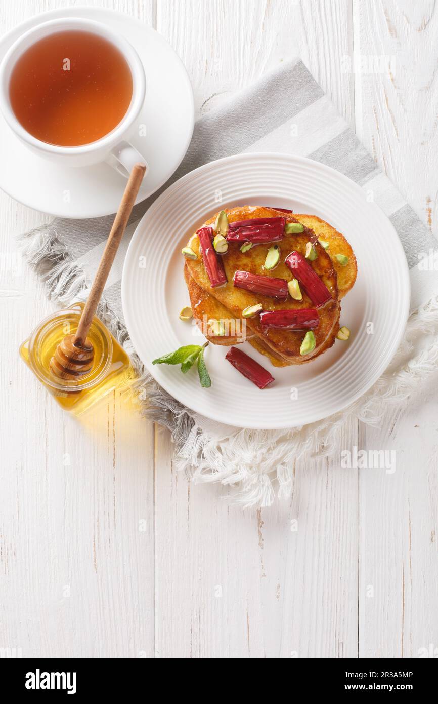 Rhubarb rôti à la vanille, toast français aux pistaches et au miel, sur une assiette sur une table en bois. Vue verticale du dessus Banque D'Images