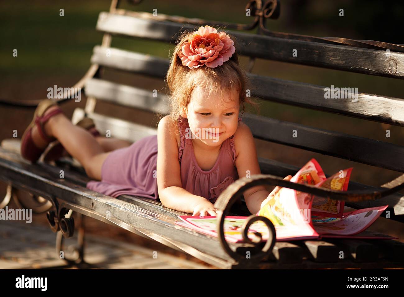 Portrait d'une petite fille lisant un livre d'enfants un banc de parc Banque D'Images
