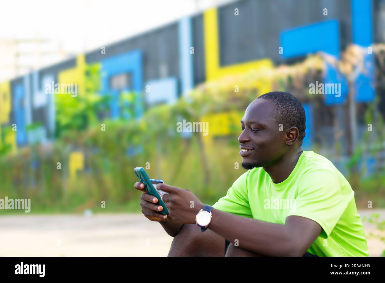 homme noir africain souriant, assis en utilisant est téléphone mobile et carte de crédit pour faire des transactions sans espèces Banque D'Images