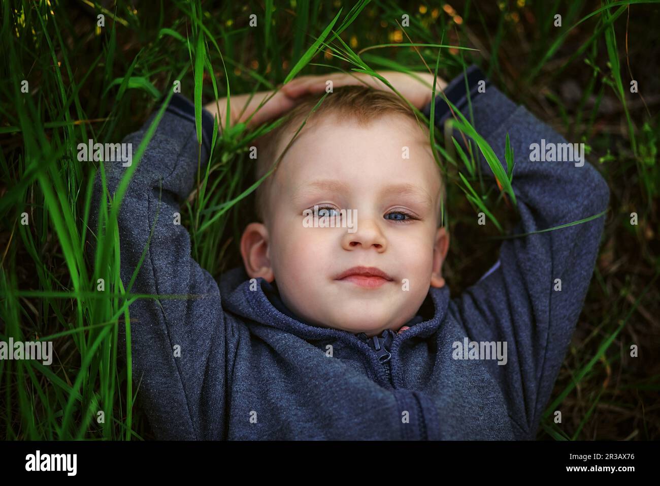 Portrait d'un petit garçon blond souriant allongé sur du vert herbe Banque D'Images