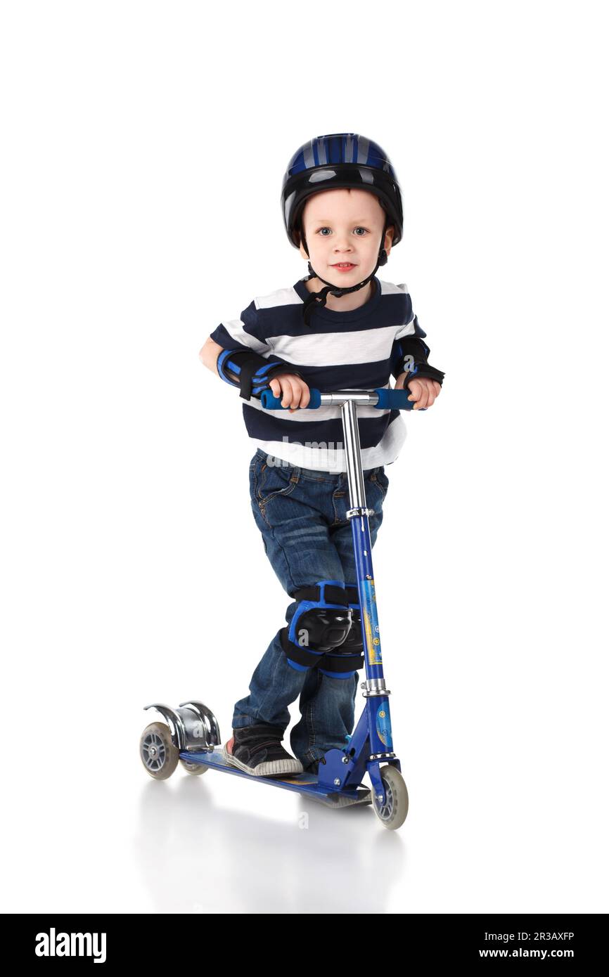 Petit garçon dans un casque de protection et dans les volants de genou et de bras portant son scooter isolé sur blanc Banque D'Images