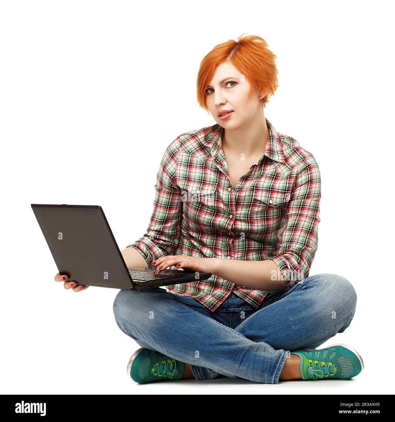 Portrait d'une jeune fille aux cheveux rouges avec un ordinateur portable assis sur le sol isolé sur le dos blanc Banque D'Images