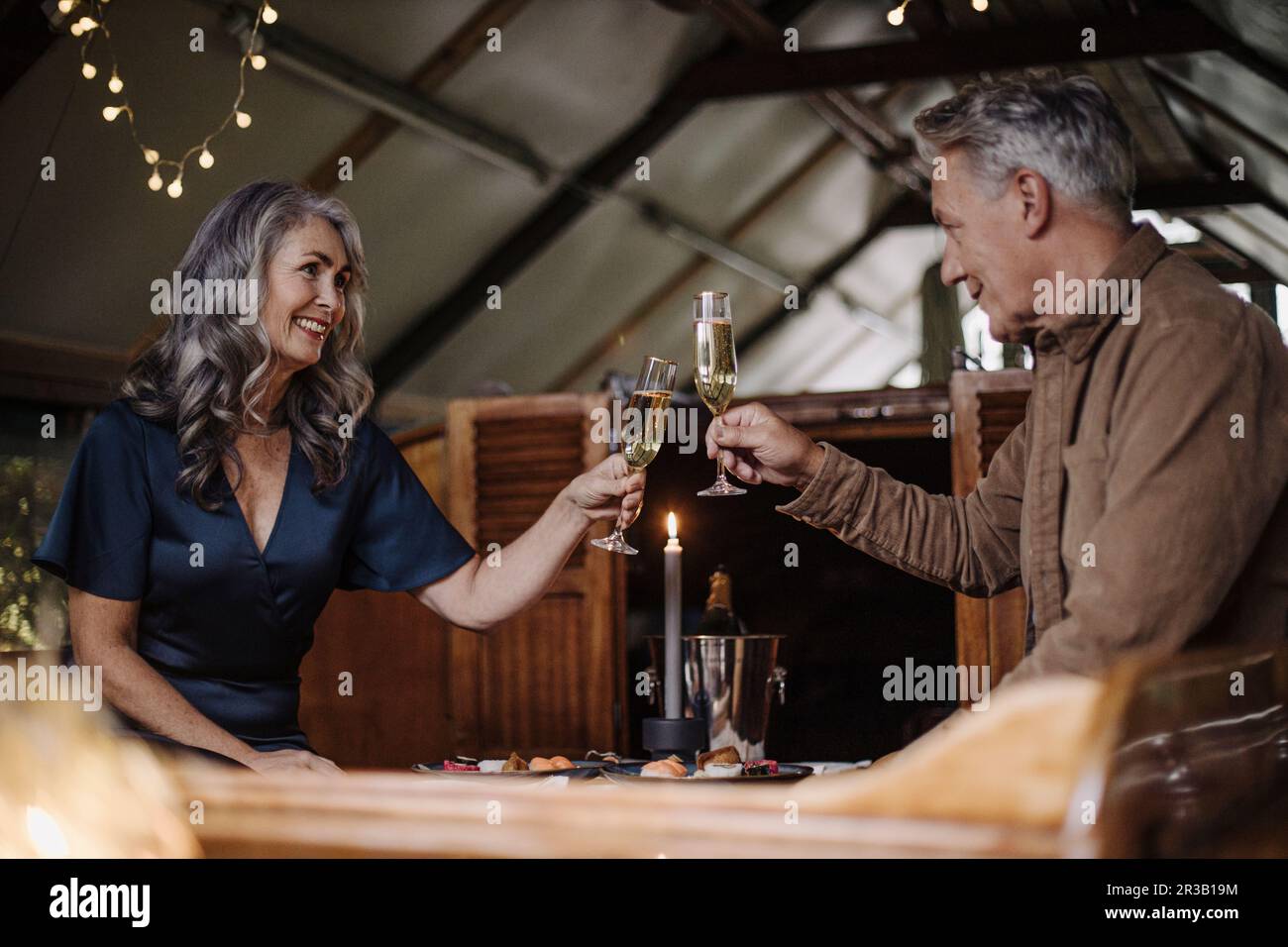 Senior couple having un dîner aux chandelles sur un bateau dans un hangar à bateaux clinking champagne glasses Banque D'Images