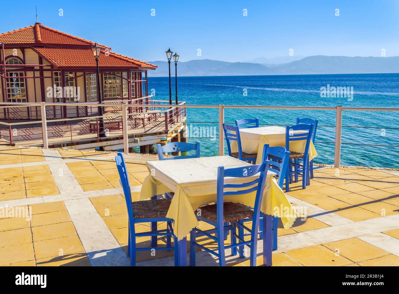 Restaurant de taverne vide en bord de mer avec chaises en bois et tables sous un soleil éclatant en été. Banque D'Images