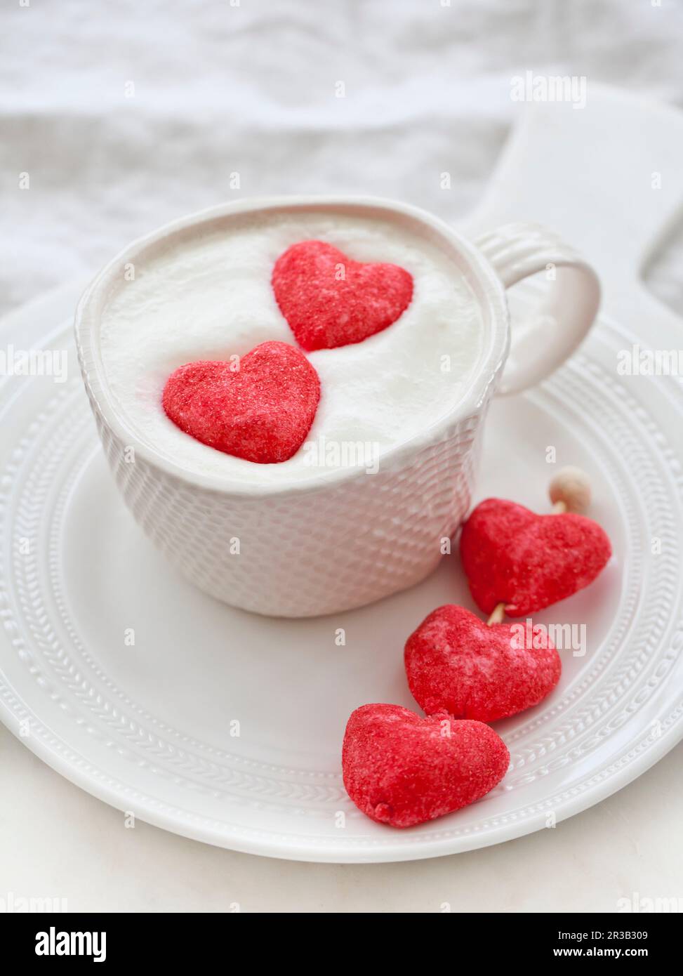 Une tasse de chocolat chaud blanc avec de la crème fouettée et deux guimauves à coeur rose Banque D'Images