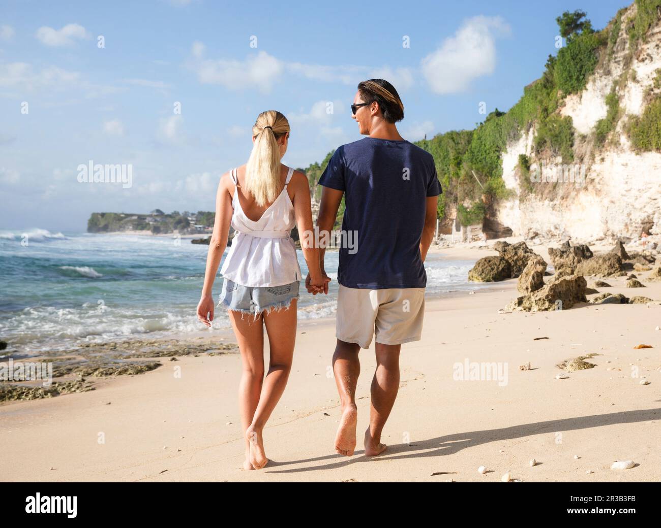 Un jeune couple heureux se tenant les mains et marchant à la plage Banque D'Images