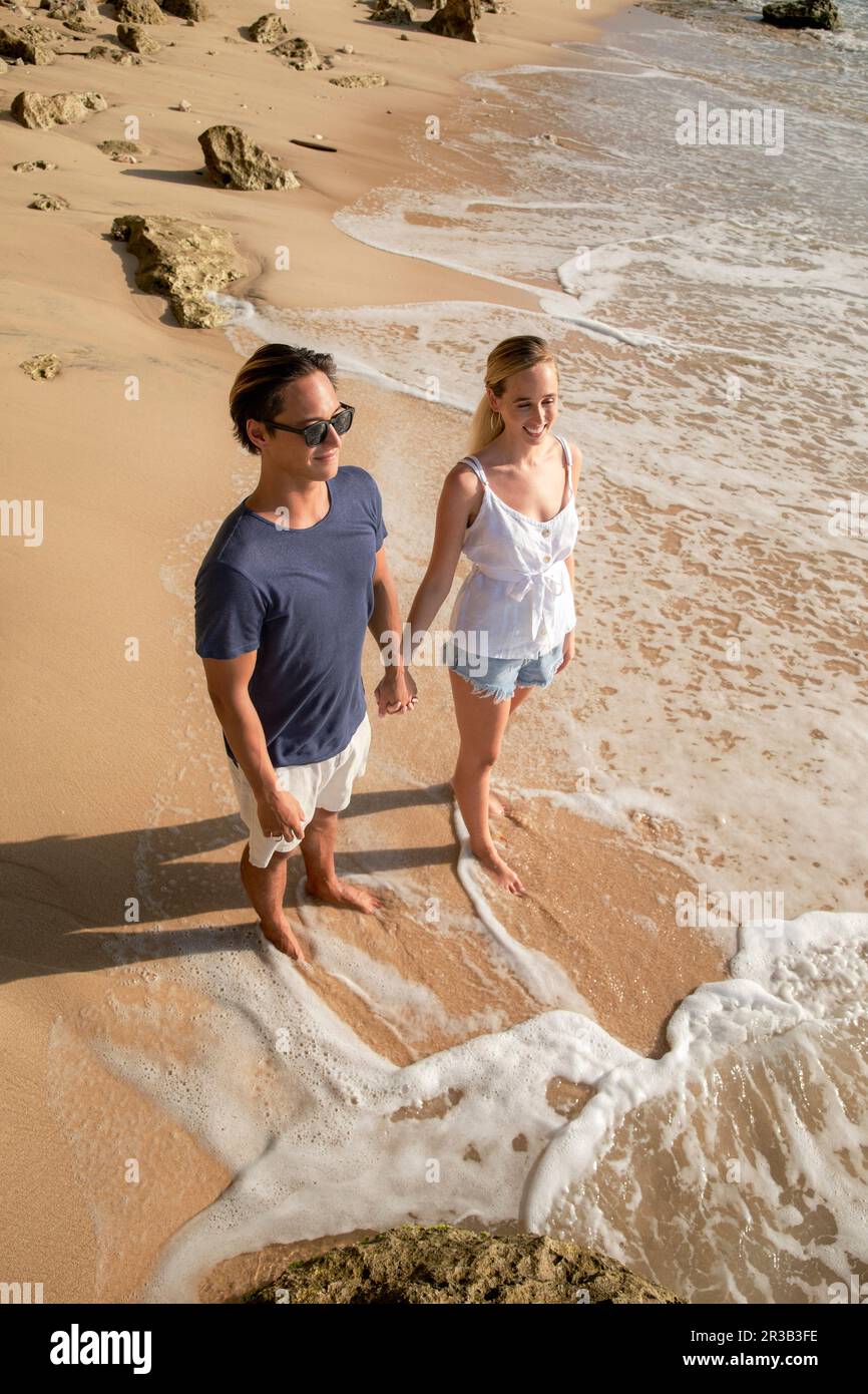 Un jeune couple heureux tenant les mains debout près du rivage à la plage Banque D'Images