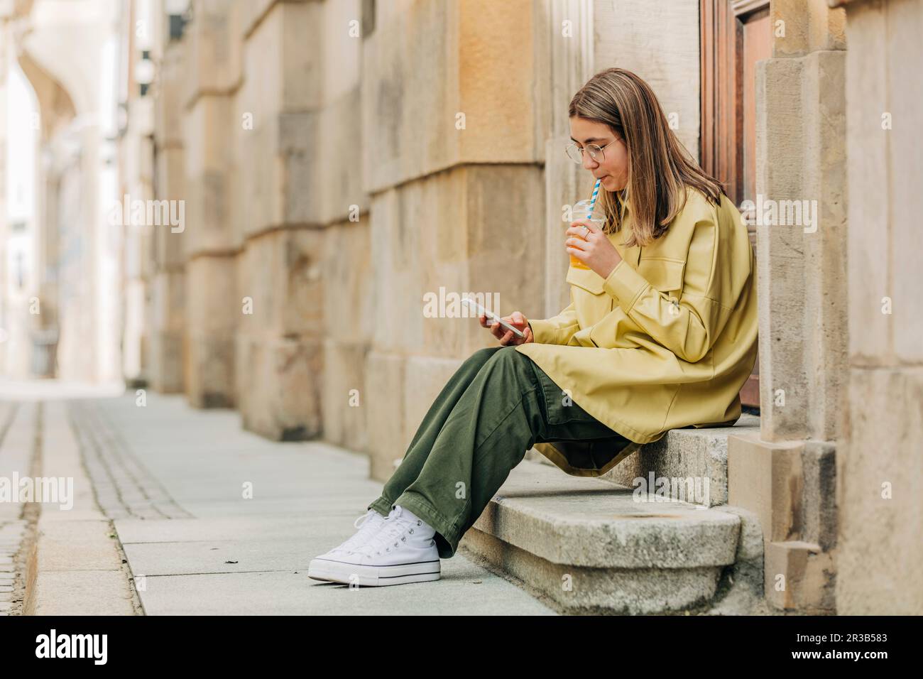 Une adolescente boit du jus et utilise un smartphone assis sur des marches Banque D'Images