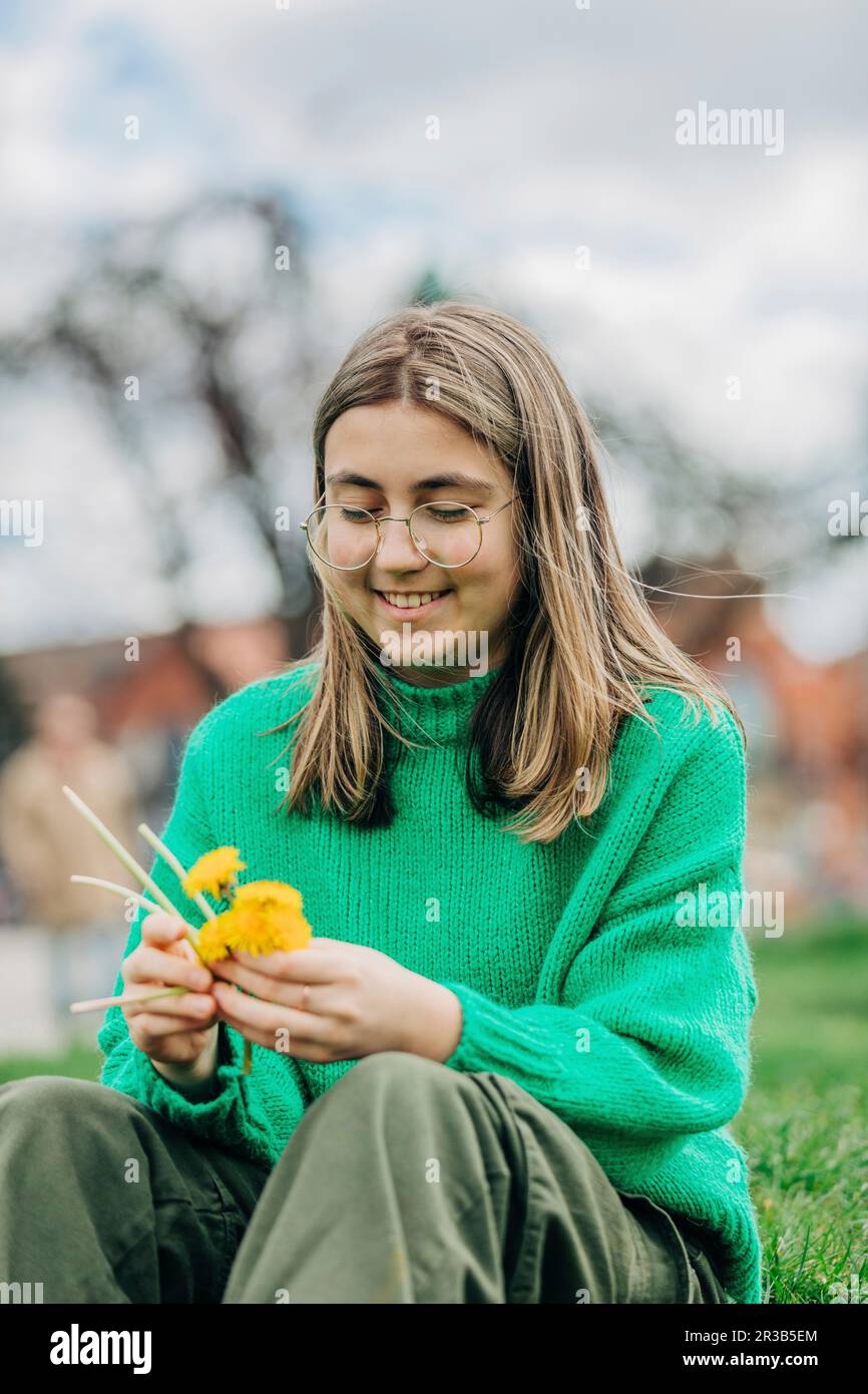 Une adolescente souriante fait une couronne avec des pissenlits jaunes assis sur l'herbe Banque D'Images