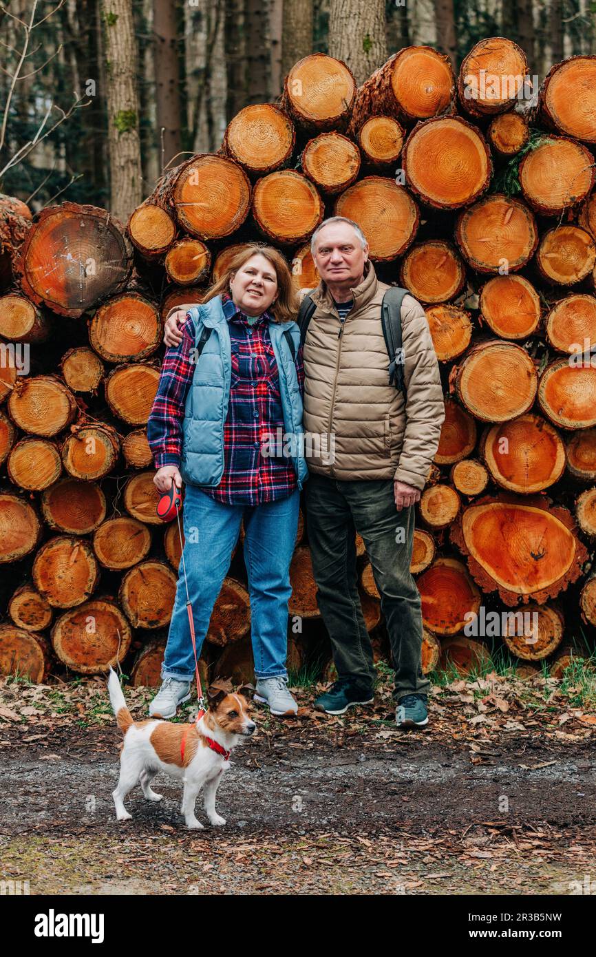 Couple senior avec un chien debout devant des grumes de pin dans la forêt Banque D'Images