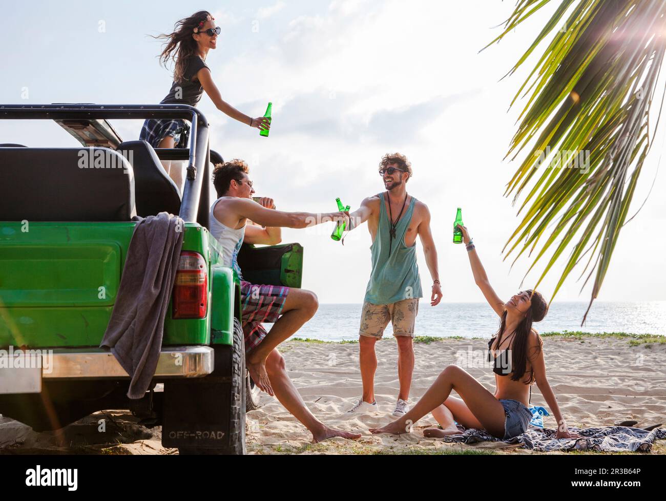 Happy Friends toaster les bouteilles de boisson avec un véhicule tout-terrain à la plage Banque D'Images
