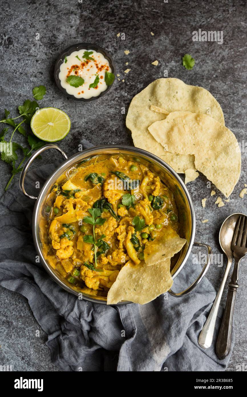 Curry de Korma au chou-fleur végétalien dans un plat de Balti servi avec des popadoms Banque D'Images