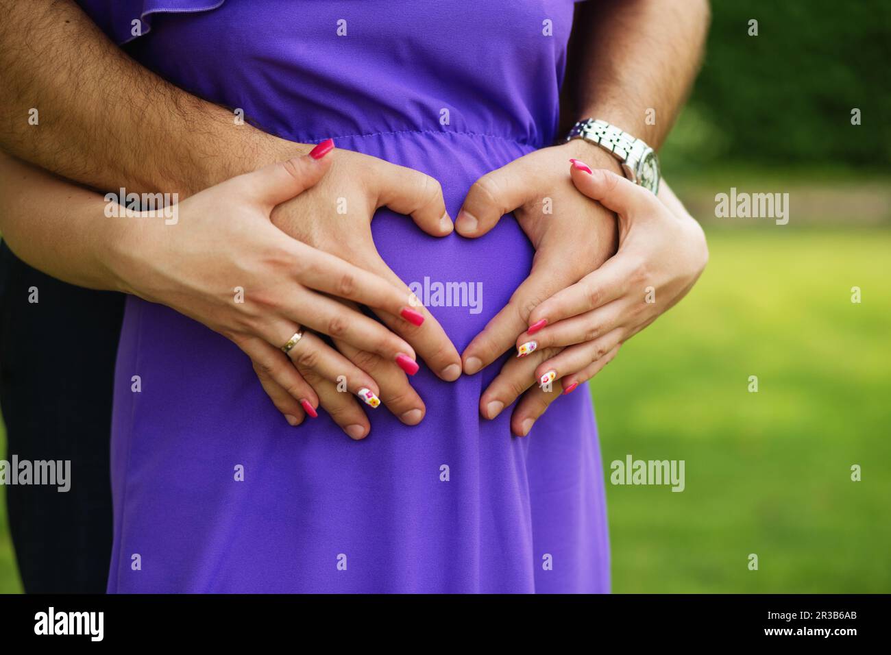 Femme enceinte et son mari tenant ses mains en forme de coeur sur la bosse de son bébé. Couple jeune exp Banque D'Images