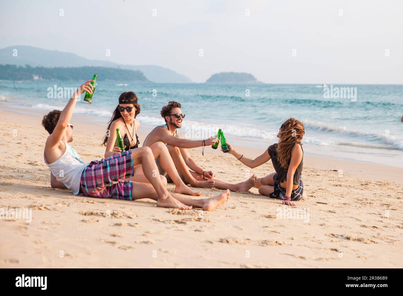 Des amis qui toastent des bouteilles de boisson assis à la plage Banque D'Images