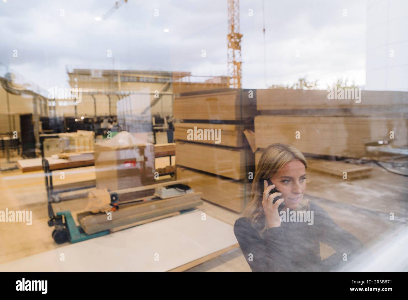 Femme d'affaires parlant sur téléphone mobile dans l'usine de menuiserie vu à travers le verre Banque D'Images