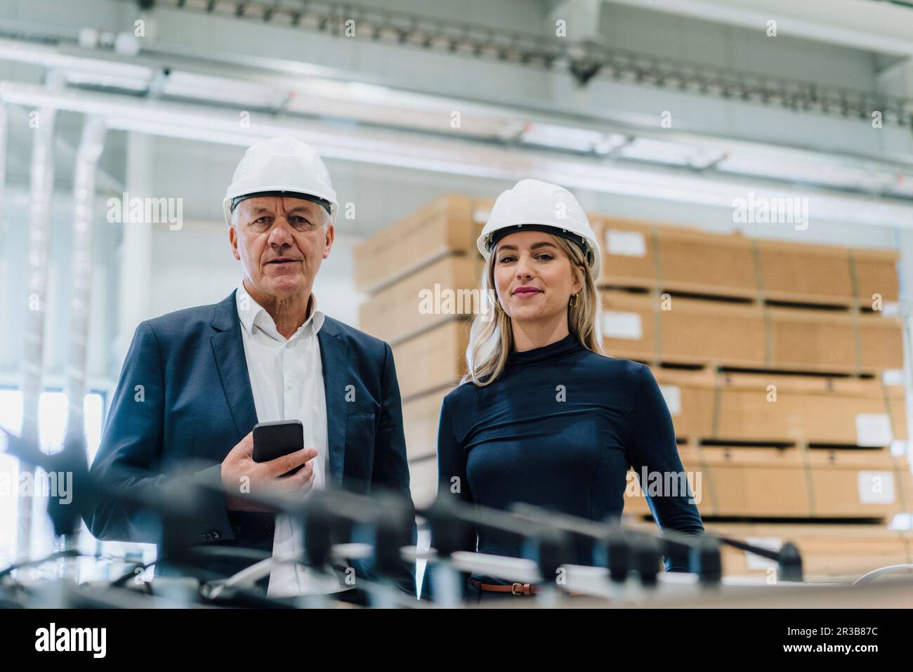 Un collègue souriant avec un homme d'affaires senior tenant un smartphone dans une usine de menuiserie Banque D'Images