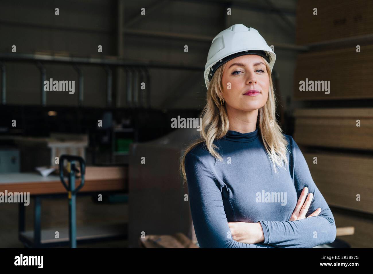 Femme d'affaires confiante aux bras croisés portant un casque de sécurité dans l'usine de menuiserie Banque D'Images