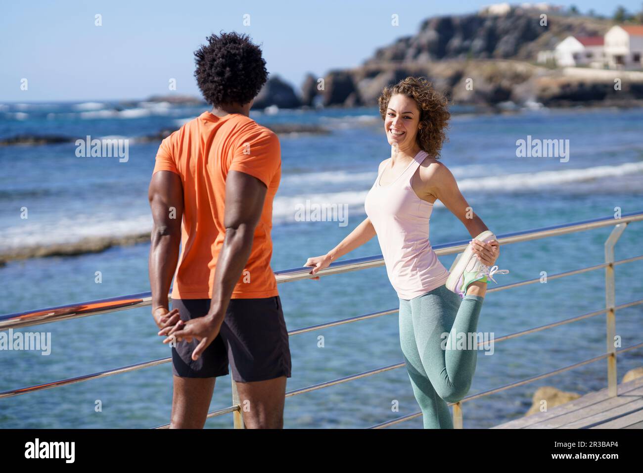 Femme souriante regardant un petit ami qui fait de l'exercice d'étirement sur la jetée dans la zone côtière Banque D'Images