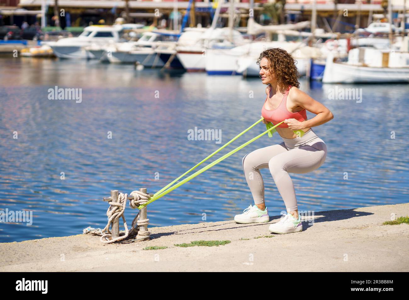 Femme faisant de l'exercice avec bande de résistance attachée sur le bollard au port Banque D'Images