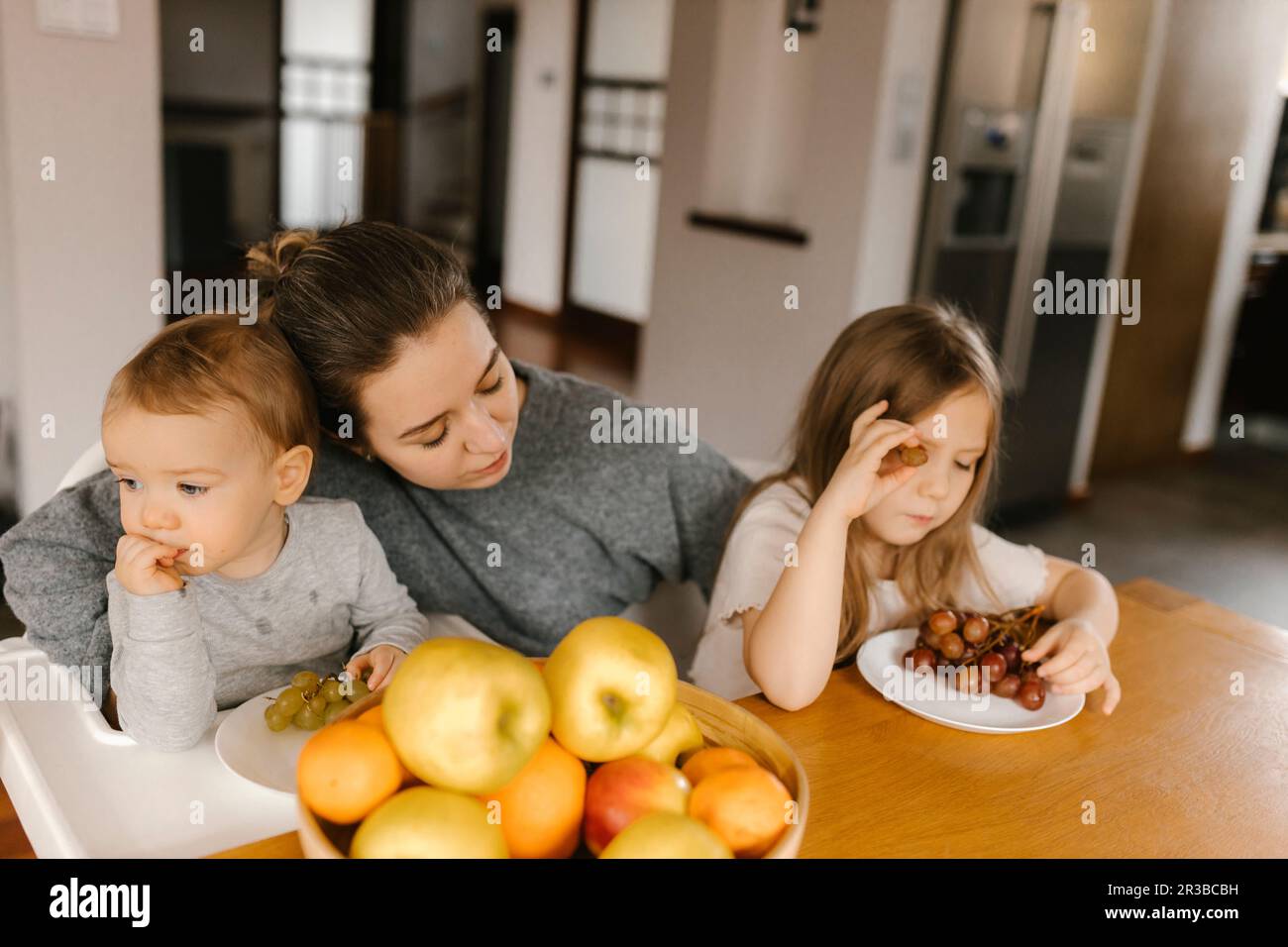 Mère avec son fils et fille mangeant des fruits frais à la maison Banque D'Images