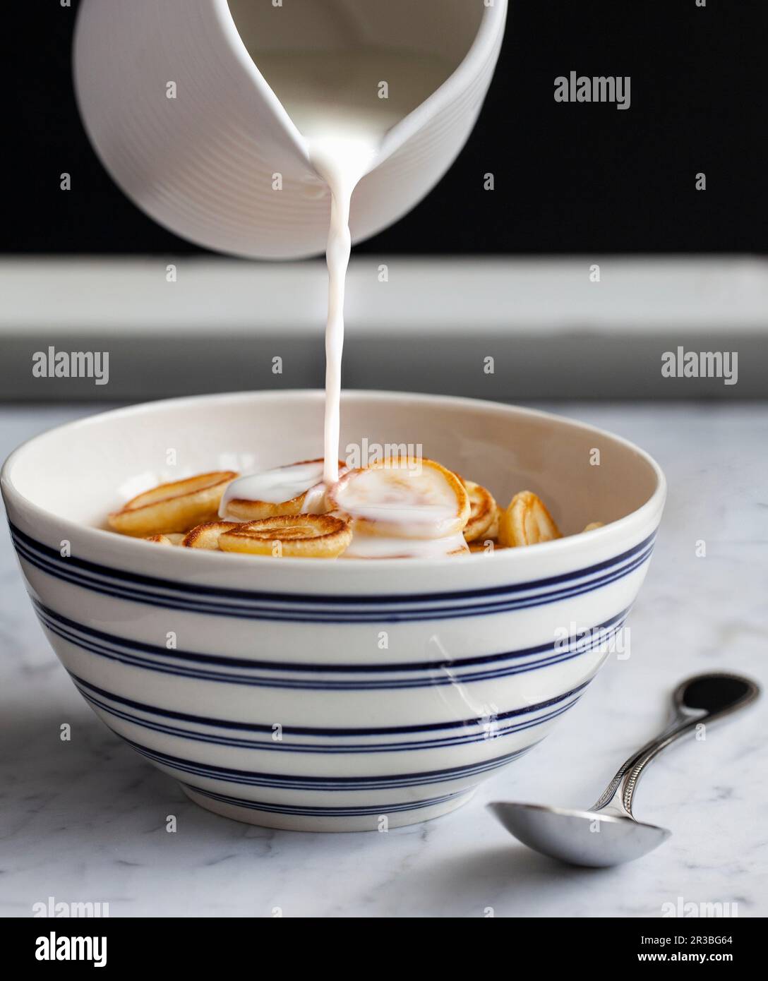 Lait versé dans un bol bleu et blanc de mini crêpes (céréales à crêpes) Banque D'Images