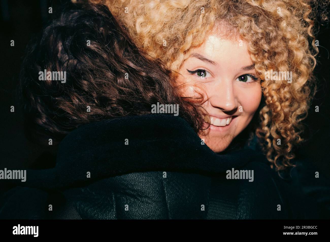 Jeune femme souriante aux cheveux bouclés qui embrassent l'ami Banque D'Images