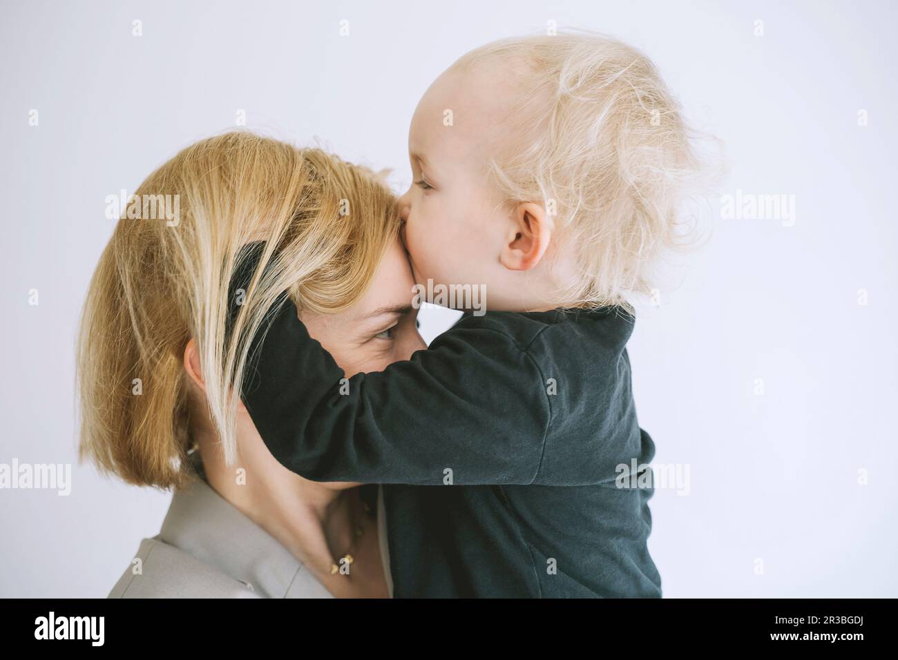 Fils embrassant sur le front de la mère sur fond blanc Banque D'Images