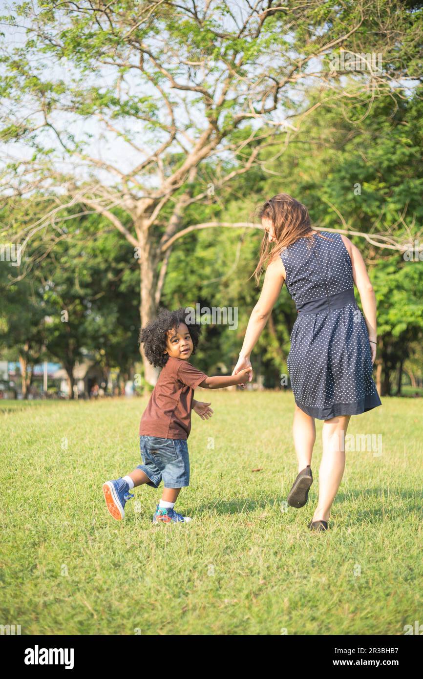 Mère et fils se tenant les mains et marchant sur l'herbe au parc Banque D'Images